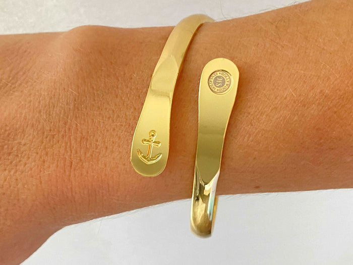 Gold anchor cuff bracelet on wrist with oval charm plate and round seal