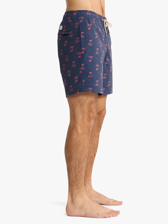 Person wearing navy blue swim shorts with red floral pattern on a white background