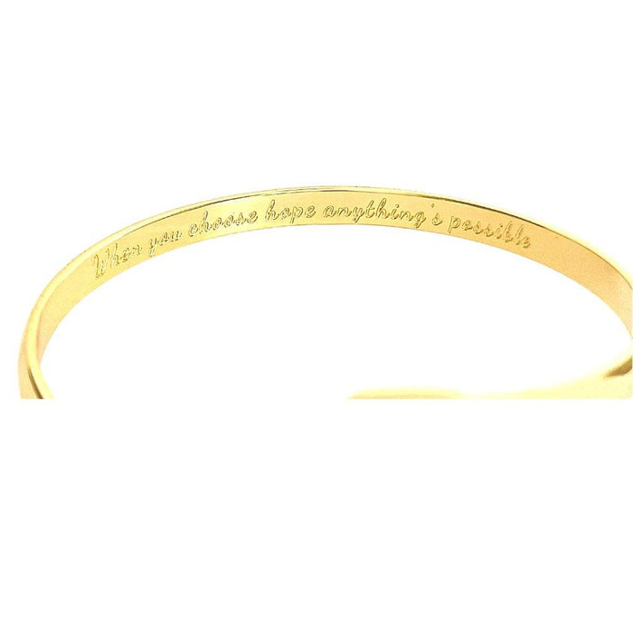 Gold engraved bracelet cuff showing inner message, ribbon emblem at center