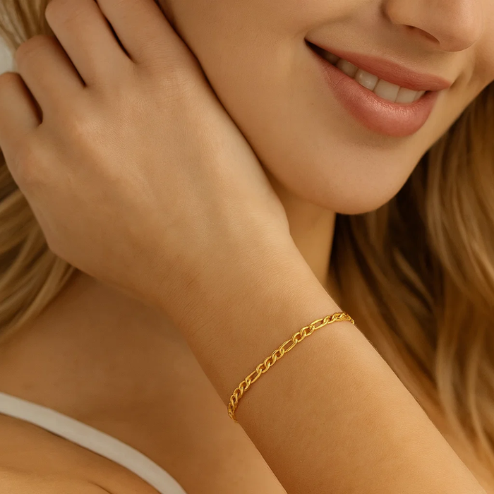 Gold figaro link bracelet on wrist, hand resting near jewelry