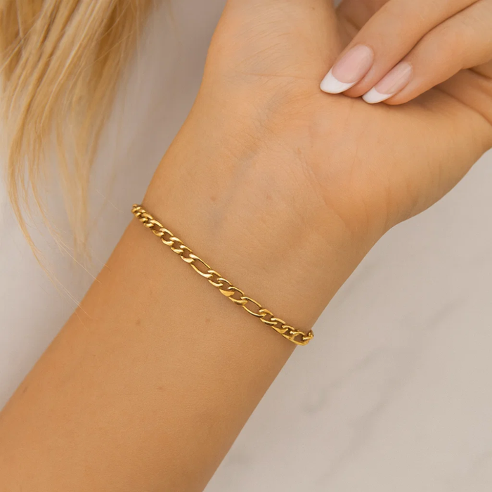 Gold figaro chain bracelet on wrist with hand and manicured nails