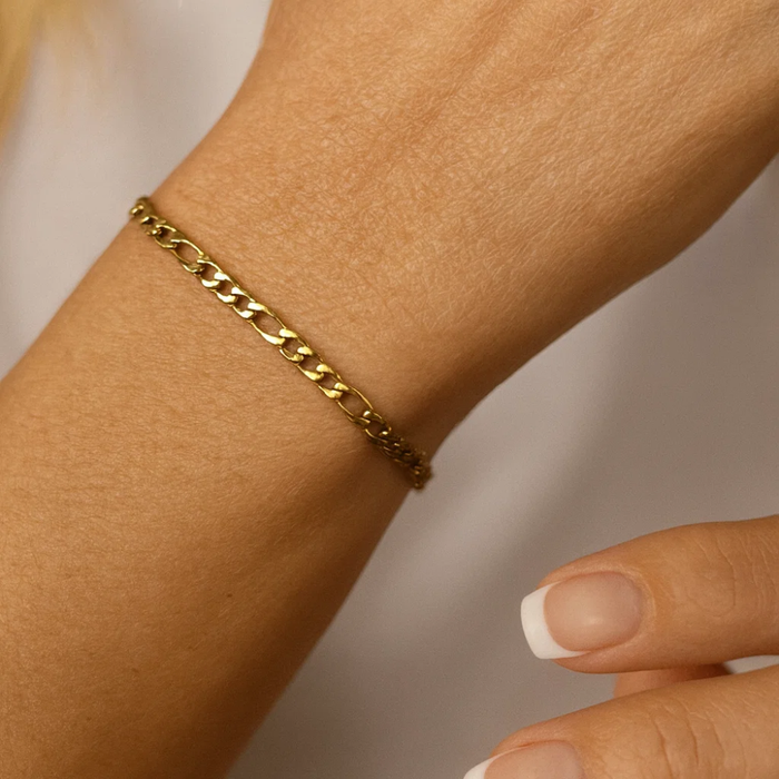 Gold figaro chain bracelet on wrist close-up with fingers nearby