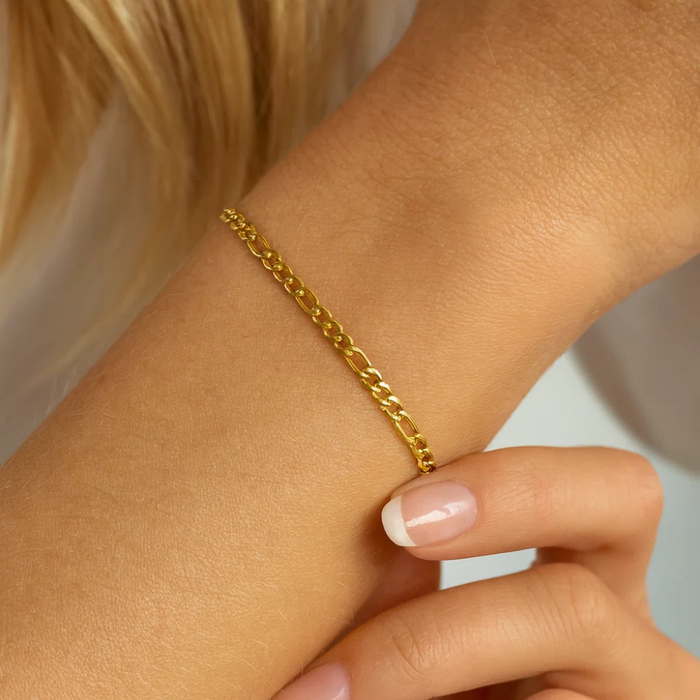 Gold figaro chain bracelet on wrist close-up with short nails