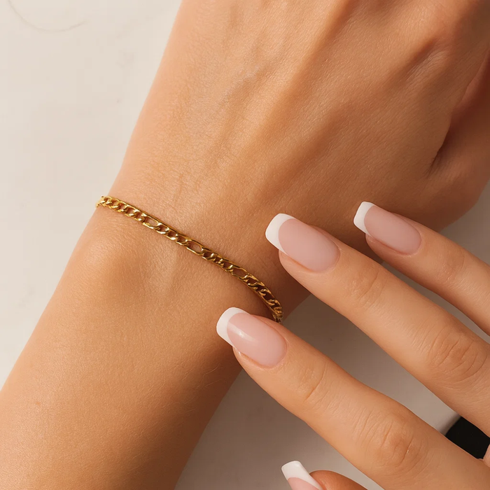 Gold chain bracelet on wrist with figaro links and manicure