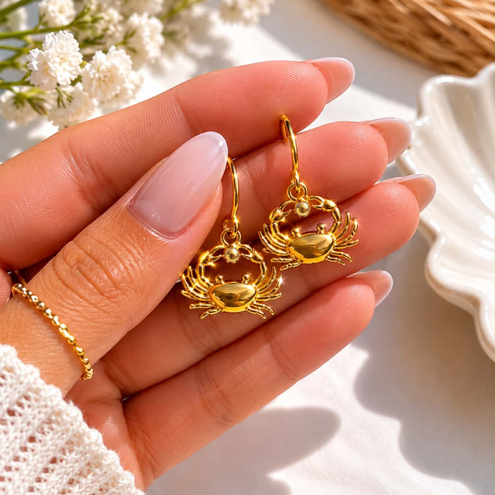 Gold crab charm dangle earrings in hand, showing hoop and crab detail