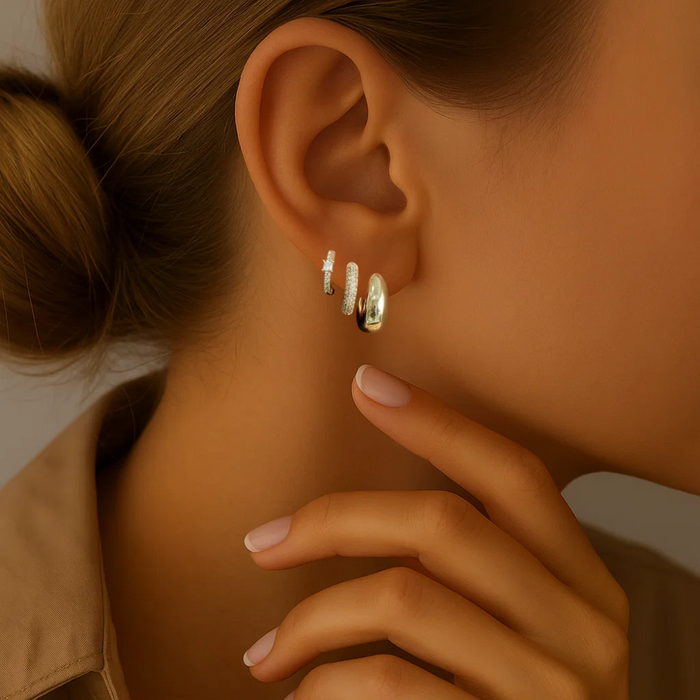 Silver-tone huggie hoop and crystal stud earrings on ear, close-up styling