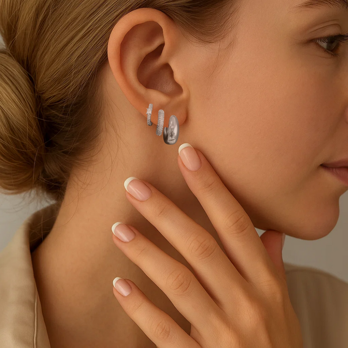 Silver-tone huggie hoops and crystal stud earrings worn on ear, side profile