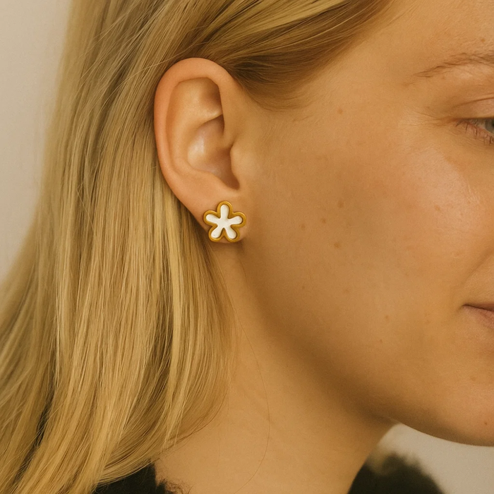 Close-up of gold flower stud earrings with white enamel centers, side view