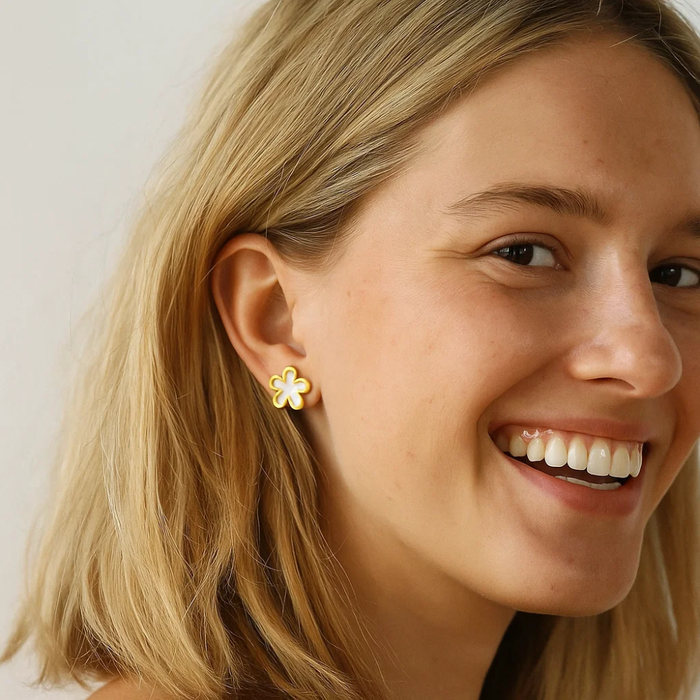 Gold flower stud earrings with white enamel centers on model's ear