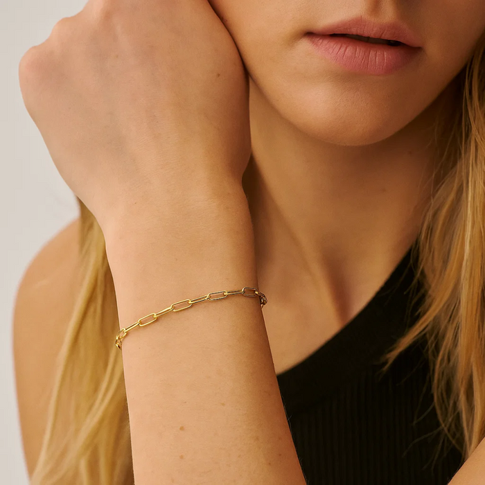 Gold paperclip link bracelet worn on wrist with chain links and small stone