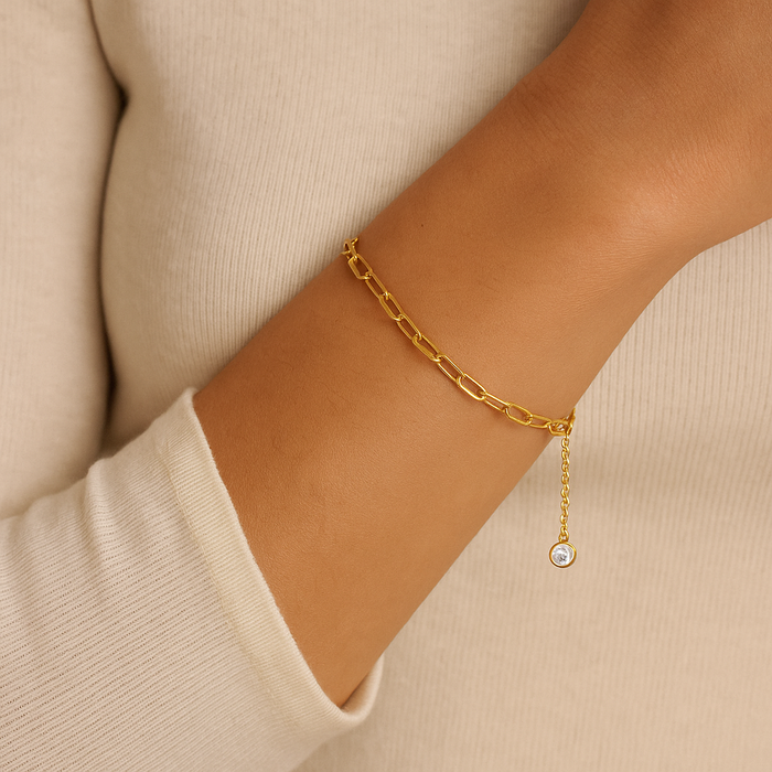 Gold paperclip link bracelet with small round stone charm, worn on wrist