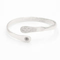 Silver infinity friendship bracelet on a flat surface, engraved infinity emblem and round logo tag.