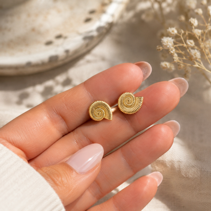 Gold spiral shell stud earrings on palm, small round swirl