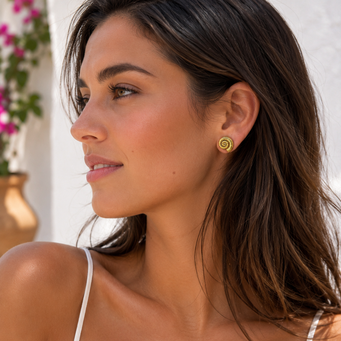Gold spiral shell stud earrings on ear, round spiral face
