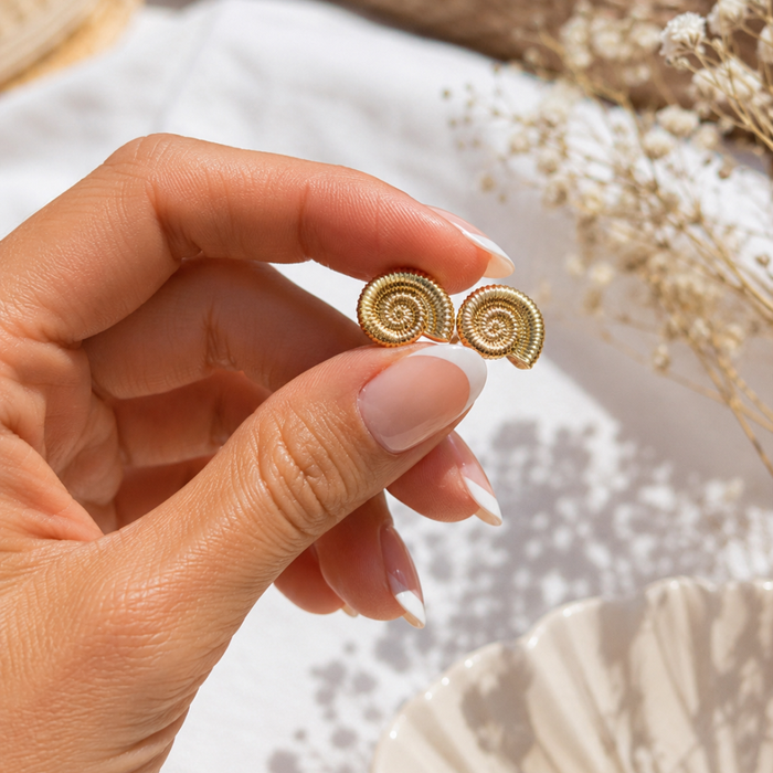 Gold spiral shell stud earrings in hand, round ribbed swirl