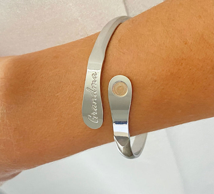 Silver-toned cuff bracelet on wrist with “Grandma” engraving and round charm