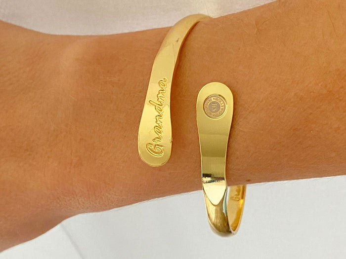 Gold-toned cuff bracelet on wrist with “Grandma” engraving and round charm