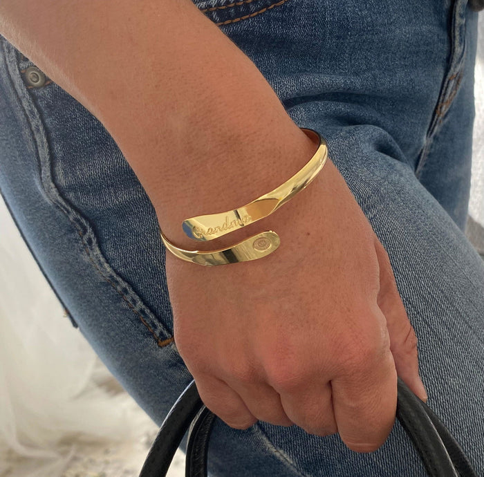 Gold-toned cuff bracelet on wrist, slim profile with “Grandma” engraving