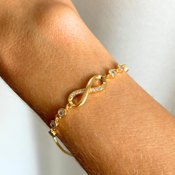 Gold infinity charm bracelet with small round crystal stones on wrist