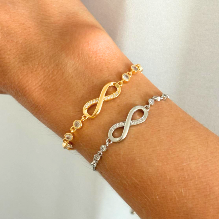 Gold and silver infinity charm bracelets with round crystal stones on wrist