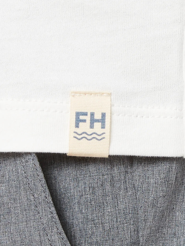 Close up of white kismet t-shirt, showing the fabric and brand logo patch. Paired with grey one pants.