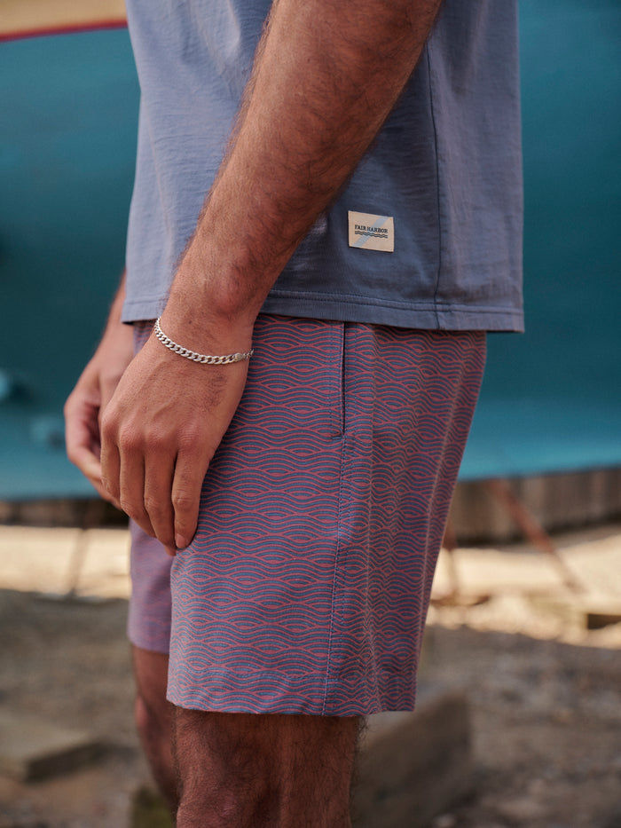 Close up of fabrics for person wearing a blue saltaire t-shirt and bayberry trunks standing in front of a colorful boat.