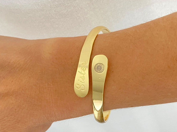 Gold sister engraved bracelet on wrist with oval nameplate and round emblem