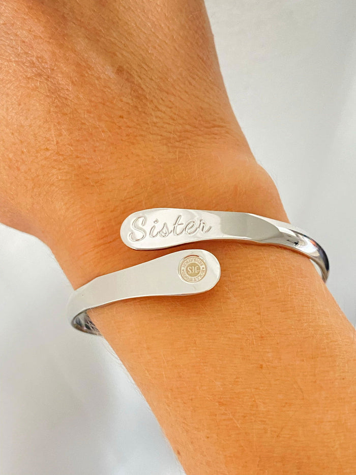 Silver sister engraved bracelet on wrist with oval nameplate and round emblem