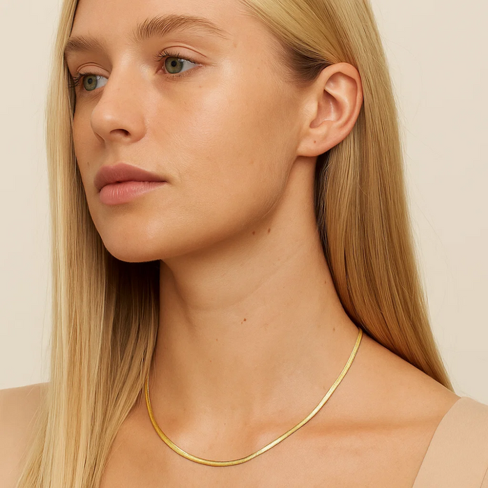 Gold snake chain necklace with slim links, worn across the neck