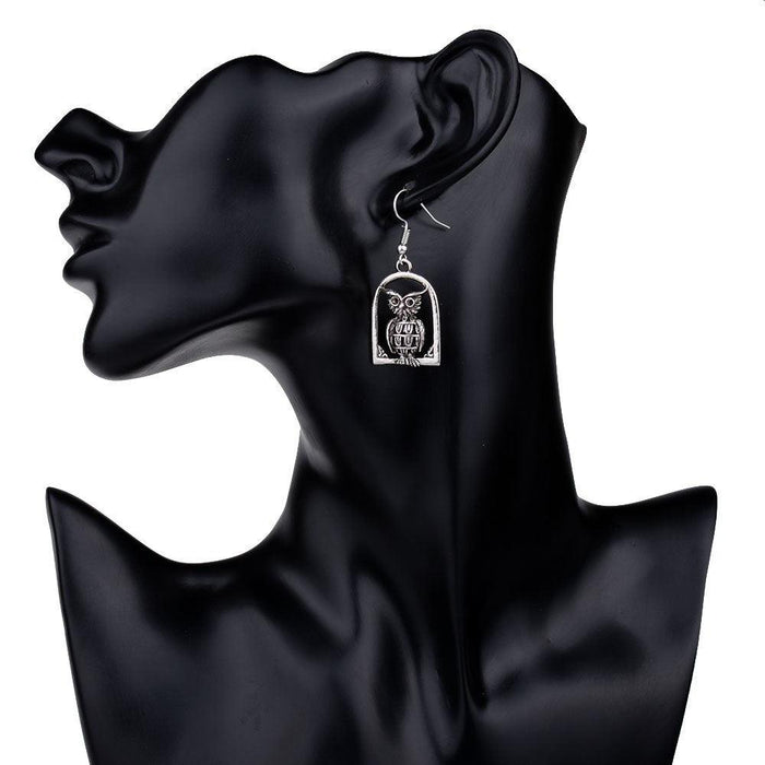 Silver-tone owl drop dangle earrings shown on a model silhouette.