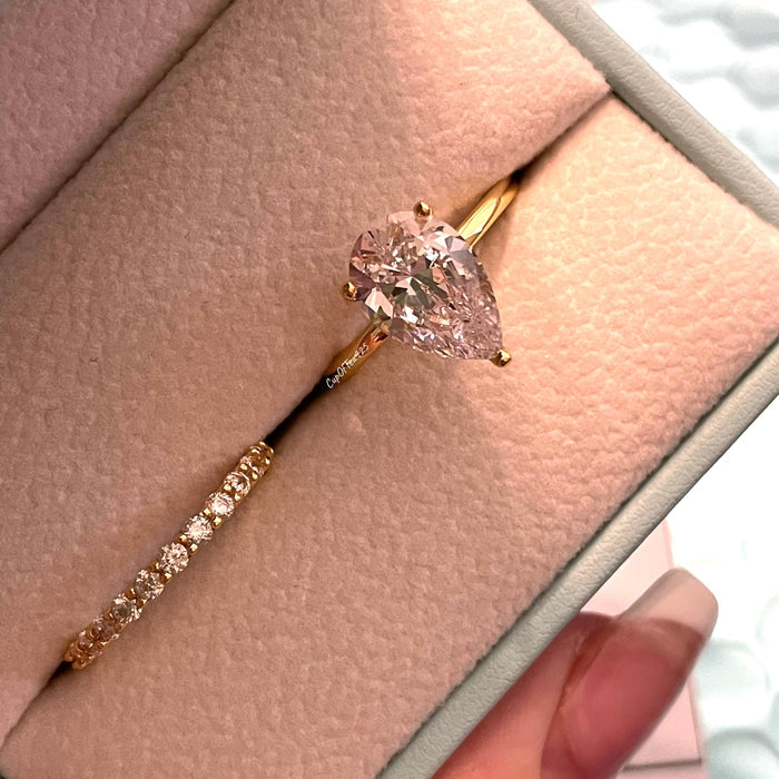 May include: A pear-shaped diamond engagement ring with a gold band. The ring is in a light blue ring box with a white interior. The diamond is clear and sparkly.