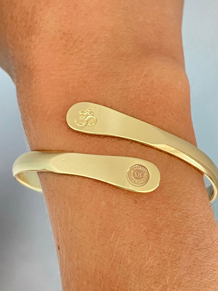 Gold yoga bracelet on wrist with engraved Om symbol and small round logo panel